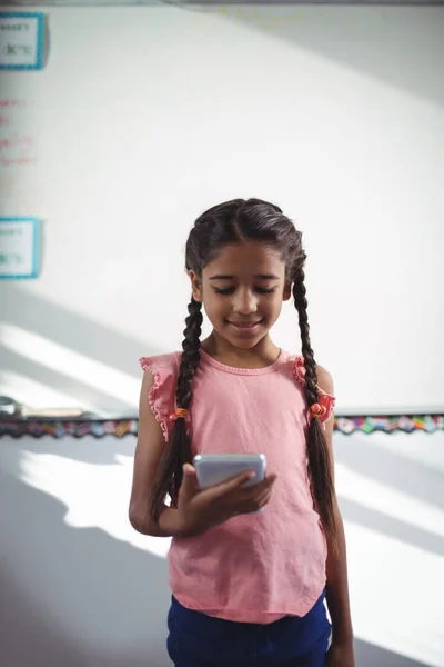 Meisje met behulp van mobiele telefoon tegen muur in de school — Stockfoto