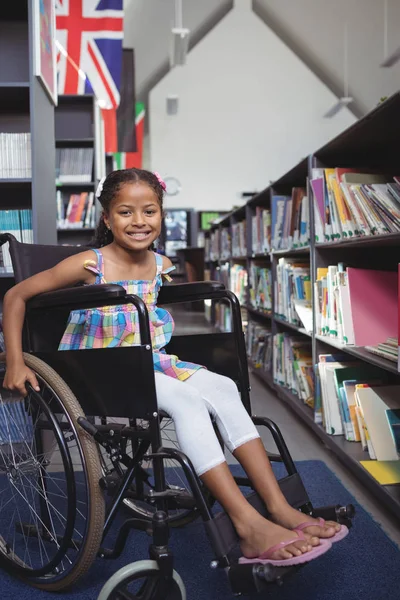 Menina sentada em cadeira de rodas na biblioteca — Fotografia de Stock