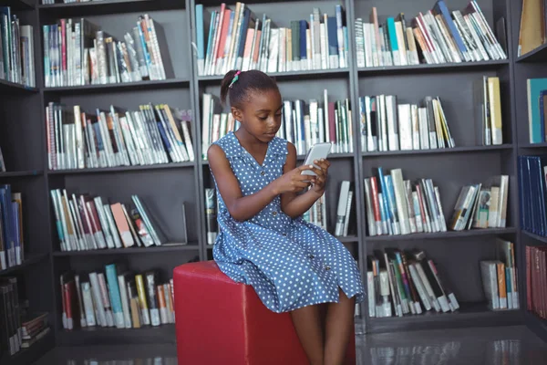 Chica usando el teléfono contra estantería en la biblioteca — Foto de Stock