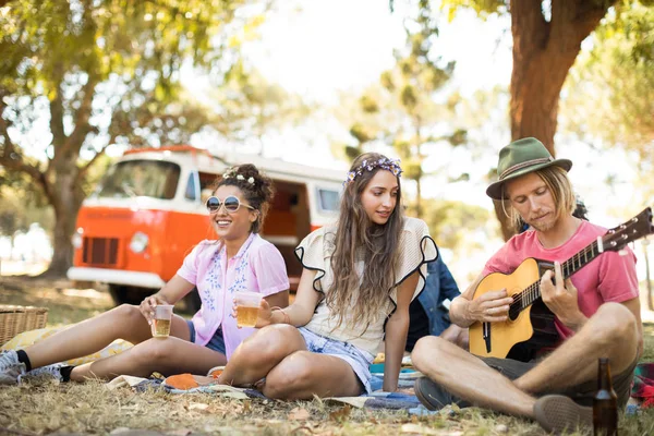 Man playing guitar by female friends having beer — Stock Photo, Image