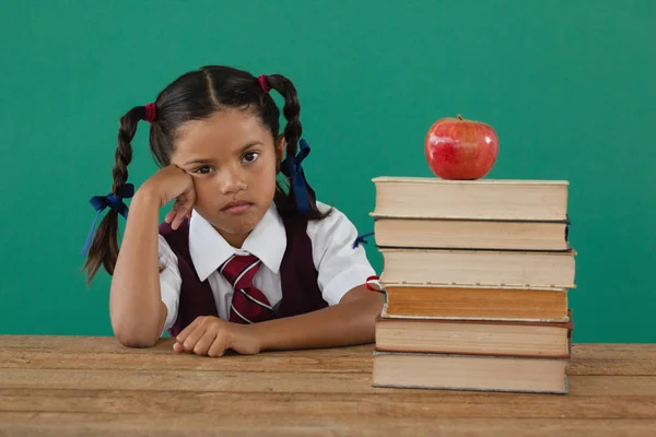 Schoolmeisje zit met gestapelde boeken — Stockfoto