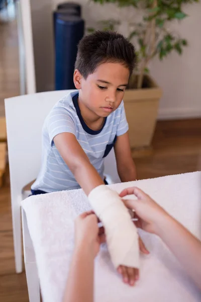 Niño mirando terapeuta envolver vendaje en la mano —  Fotos de Stock