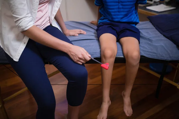 Terapeut undersökande pojke med reflex hammare på knä — Stockfoto