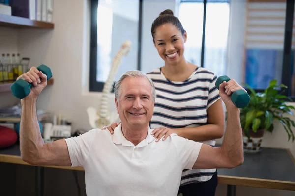 Doctor standing with patient lifting dumbbells — Stock Photo, Image