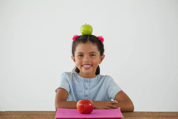 Школьница сидит с зеленым яблоком на голове — стоковое фото