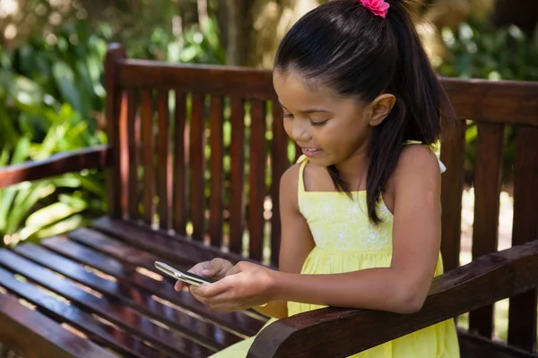 Menina usando celular no banco de madeira — Fotografia de Stock