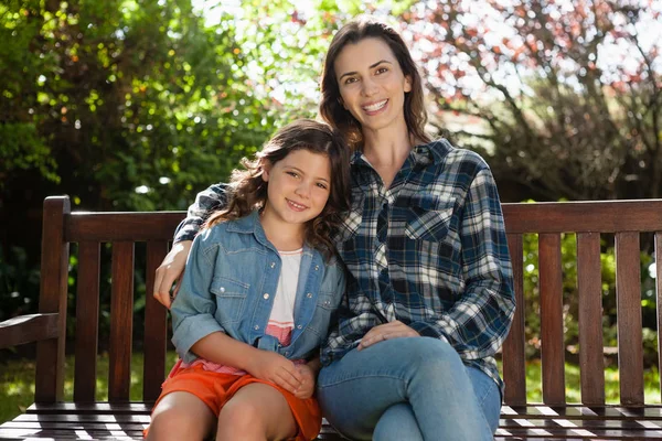 Woman and daughter sitting on wooden bench — Stock Photo, Image