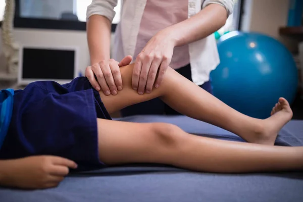 Terapeut masíruje koleno chlapce, ležící na posteli — Stock fotografie