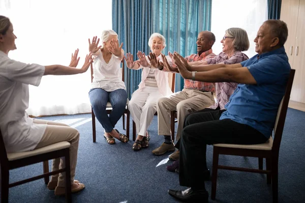 Жінка-лікар і літні люди, що займаються на стільцях — стокове фото