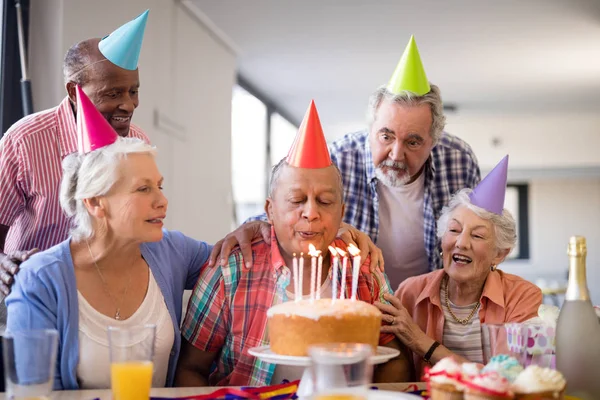 Vrienden op zoek naar senior man waait birthday kaarsen — Stockfoto