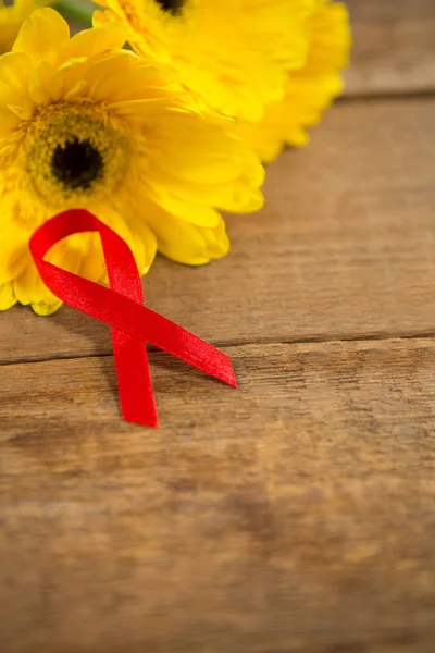 Czerwone wstążki świadomości Aids przez kwiaty gerbera — Zdjęcie stockowe