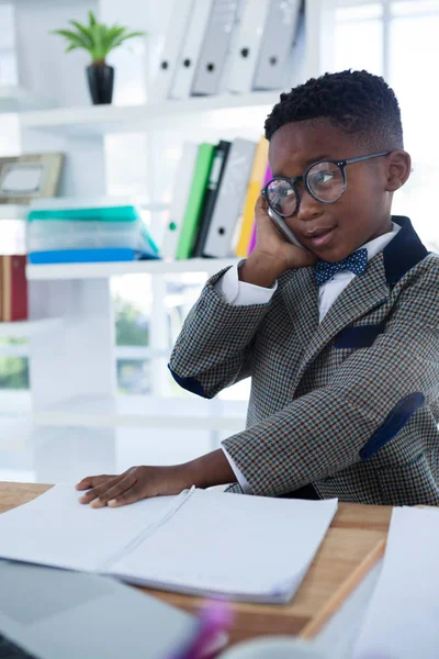 Businessman using mobile phone and reading book at desk — Stock Photo, Image