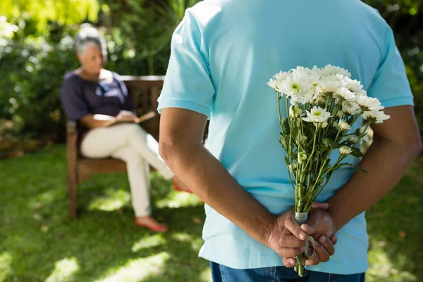 Homem sênior escondendo flores nas costas — Fotografia de Stock