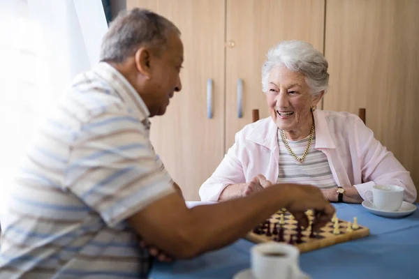 Anziani maschi e femmine che giocano a scacchi a tavola — Foto Stock