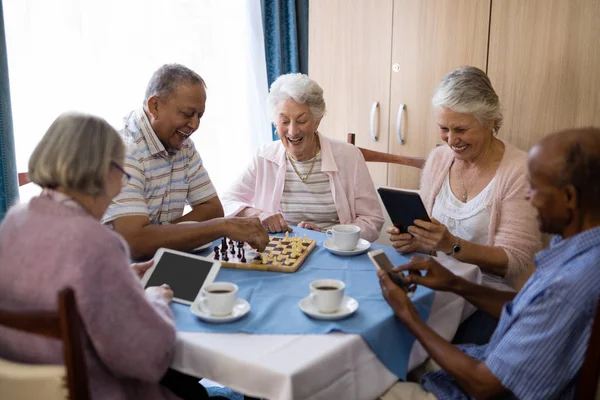 Amigos seniores jogando xadrez e usando tecnologia — Fotografia de Stock