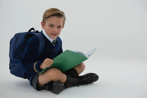 Schüler liest Buch, während er auf weißem Hintergrund sitzt — Stockfoto