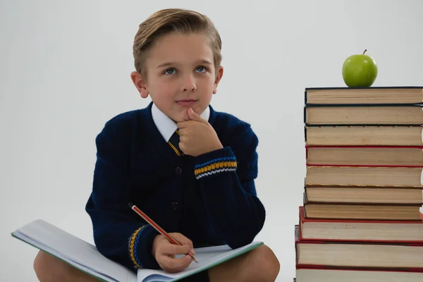 Schoolboy fazendo seu dever de casa enquanto sentado ao lado de pilha de livros — Fotografia de Stock