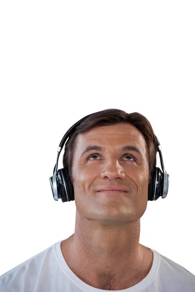 Hombre sonriente escuchando música a través de auriculares mientras mira hacia arriba — Foto de Stock