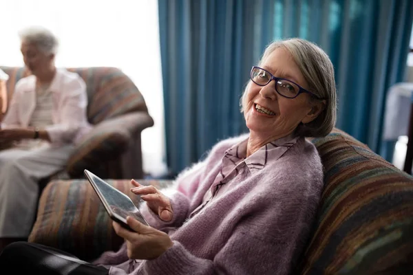 Senior kvinna sitter med surfplatta på fåtölj — Stockfoto