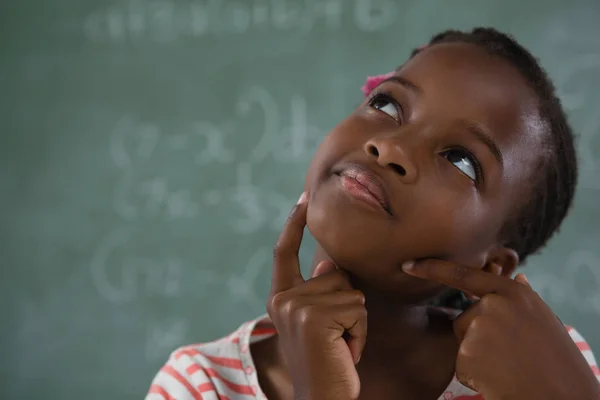 Schoolgirl sitting against chalkboard — Stock Photo, Image