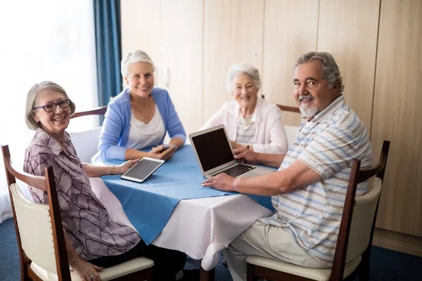 Senioren met technologieën aan tafel zitten — Stockfoto