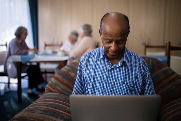 Uomo anziano utilizzando il computer portatile mentre seduto sul divano — Foto Stock