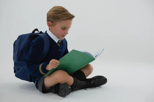 Schüler liest Buch, während er auf weißem Hintergrund sitzt — Stockfoto