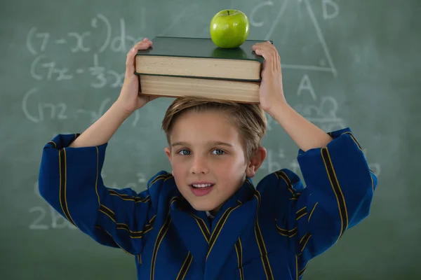 Schoolboy segurando pilha de livros com maçã contra quadro — Fotografia de Stock