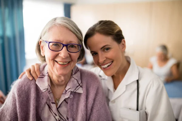 Vrouwelijke arts staande arm rond senior vrouw — Stockfoto