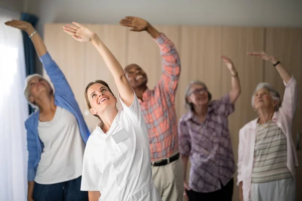 Female doctor and seniors exercising with arms raised — Stock Photo, Image