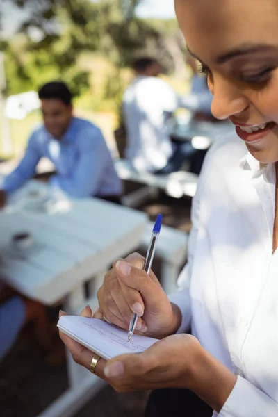 Una camarera sonriente escribiendo una orden en el bloc de notas — Foto de Stock