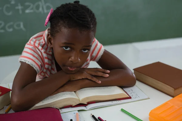 Schoolmeisje ontspannen op een open boek in klas — Stockfoto