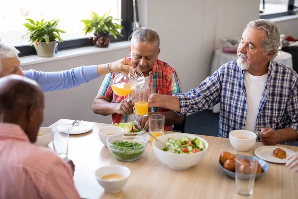 Mulher sênior servindo bebida para amigos na mesa — Fotografia de Stock