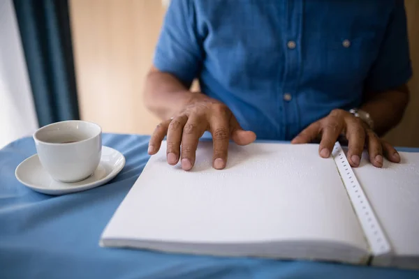 Hombre mayor leyendo libro por taza de café en la mesa —  Fotos de Stock