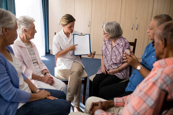 Dokter wijzen terwijl het Klembord uit te leggen aan senioren — Stockfoto