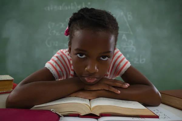 Schoolgirl relaxing on open book in classroom — Stock Photo, Image