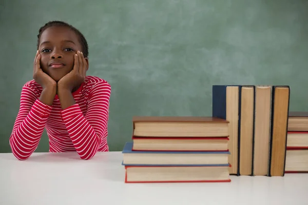 Schoolmeisje naast de stapel boeken zit — Stockfoto