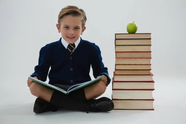 Schoolboy ler livro enquanto sentado ao lado de pilha de livros — Fotografia de Stock