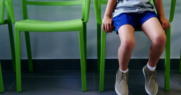 Rozrušený chlapec sedí na židli v nemocniční chodbě — Stock video