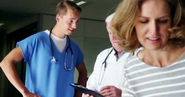 Enfermera y médico discutiendo sobre portapapeles en el pasillo — Vídeos de Stock