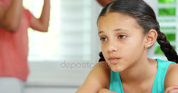 Ledsen flicka sitter vid bordet medan föräldrar argumentera — Stockvideo