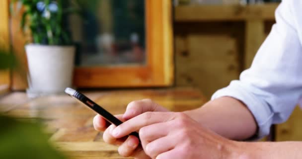 Человек сидит за столом и использует мобильный телефон — стоковое видео