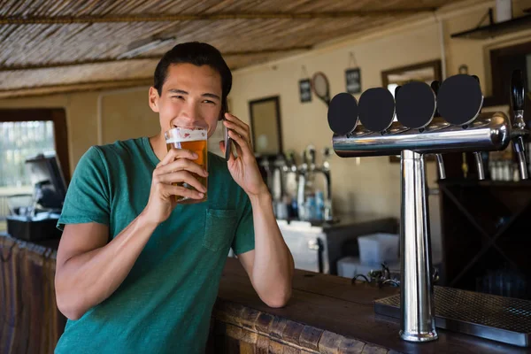 Homme buvant de la bière tout en parlant au téléphone — Photo