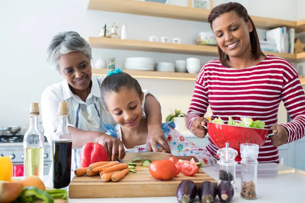 Grandmother assisting granddaughter to chop vegetables — Stock Photo, Image
