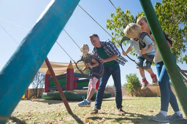 Parents ludiques balançant les enfants à l'aire de jeux — Photo