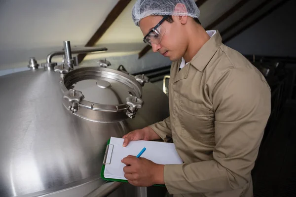Worker writing on clipboard by storage tank — Stock Photo, Image