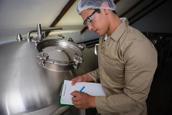 Trabajador escribiendo en el portapapeles por tanque de almacenamiento —  Fotos de Stock