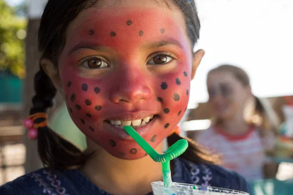 Chica con la cara pintura bebiendo en el parque — Foto de Stock