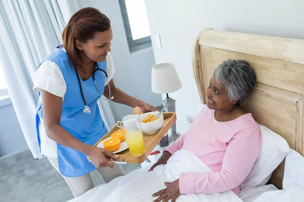 Médico que sirve el desayuno a la mujer mayor en la cama —  Fotos de Stock