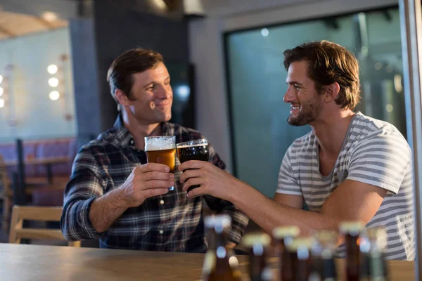 Amigos felizes brindando cerveja no bar — Fotografia de Stock